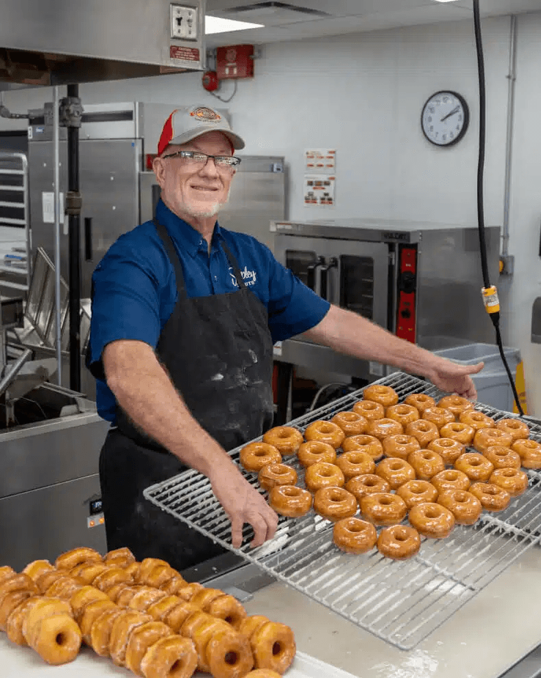 Shipley employee with rack full of original glazed donuts
